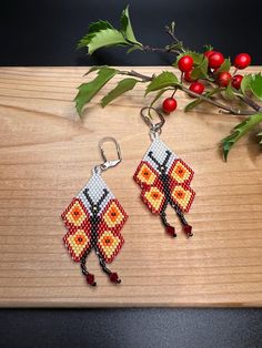 a pair of beaded earrings sitting on top of a wooden table next to berries