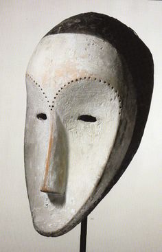 a white mask with a brown nose on a black stand in front of a wall