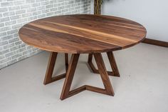 a round wooden table sitting in front of a brick wall next to a potted plant