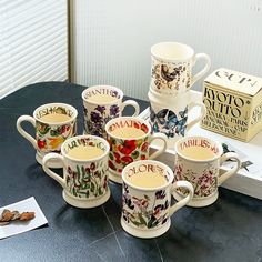 six coffee mugs sitting on top of a table next to a box of cookies