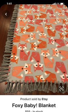 an orange and grey blanket with red foxes on the front is laying on a wooden floor