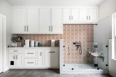 a kitchen with white cabinets and tile backsplashing on the countertop, along with a tiled shower stall