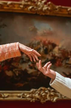 two hands reaching out towards each other in front of a painting with gold trimmings