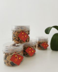 four glass jars filled with cookies on top of a white table next to a green plant