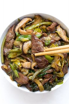 stir fry with beef and vegetables in a white bowl, chopsticks on the side