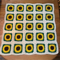 a crocheted blanket with sunflowers on it sitting on top of a wooden table