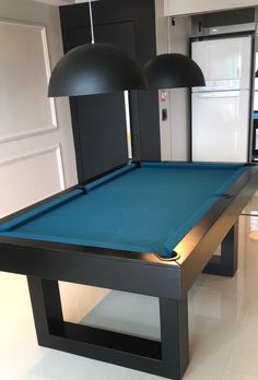 a pool table in the middle of a room with two lights on it and a refrigerator behind it