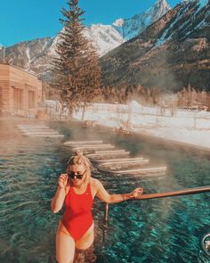 a woman in a red swimsuit standing next to a body of water with mountains in the background