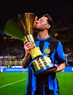 a soccer player kissing the trophy in front of his face while standing on a field