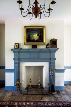 a fireplace with a painting on the wall above it and a chandelier hanging from the ceiling