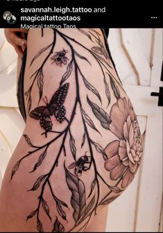 the back of a woman's thigh with tattoos on it and flowers in the background