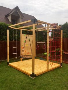 a wooden play structure in the backyard with climbing ropes and balls on it's sides