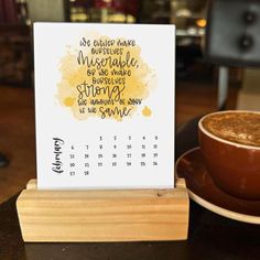 a cup of coffee sitting on top of a wooden table next to a calendar with writing