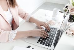 a woman is typing on her laptop while sitting at a desk with flowers in the background