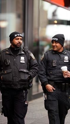 two police officers walking down the street with coffee in their hands and talking to each other