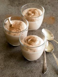 three glasses filled with dessert sitting on top of a table next to silver spoons