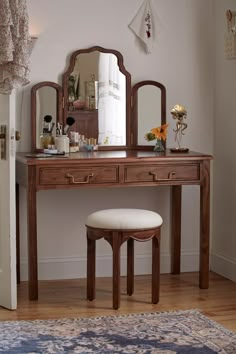 a dressing table with mirror and stool in front of it on top of a hard wood floor