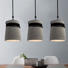 three pendant lights hanging over a dining room table with chairs and a vase on it