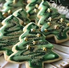 decorated cookies with green icing and gold stars are on a white platter in the shape of christmas trees