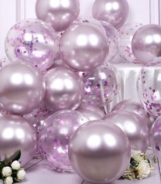 a bunch of balloons that are sitting on the ground in front of a wall with flowers