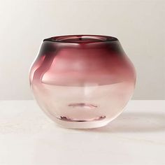 a pink glass vase sitting on top of a white table next to a gray wall