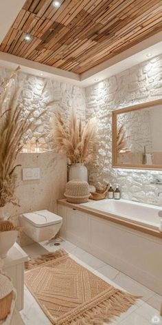 a white bathroom with stone walls and wood ceilinging is pictured in this image, there are plants on the counter next to the bathtub