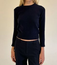 a woman standing in front of a white wall wearing black pants and a blue sweater