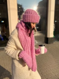 a woman in a pink hat and scarf holding a coffee cup