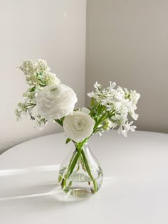 white flowers are in a clear vase on a table