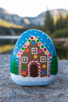 a painted rock with a gingerbread house on it's side and mountains in the background