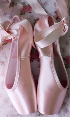 two pairs of ballet shoes with ribbons tied around their ankles on a floral sheeted surface