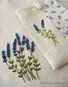 two embroidered napkins with blue flowers on them sitting next to each other, one in front of the other