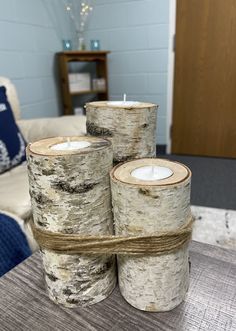 three white candles sitting on top of wooden logs