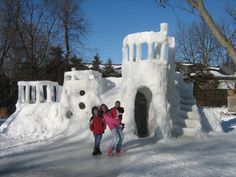 two girls standing in front of an ice castle with snow on the ground and trees behind them