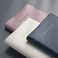 three different colored leather cases sitting next to each other on top of a gray surface