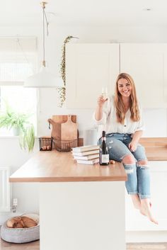 a woman sitting on top of a kitchen counter holding a bottle of wine and smiling