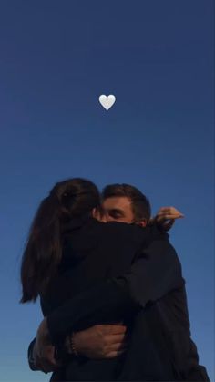 two people hugging each other with a heart shaped object in the sky behind them on a sunny day