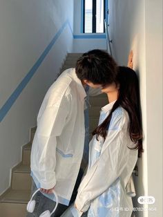 a man and woman are kissing on the stairs in front of a window with blue trim