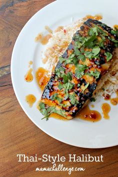 a white plate topped with fish and rice on top of a wooden table next to a fork