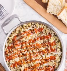 a large pot filled with pasta and sauce next to bread