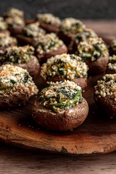 several stuffed mushrooms on a wooden platter with cheese and spinach sprinkled on top