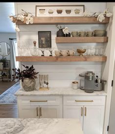 a kitchen with white cabinets and marble counter tops, gold accents on the shelves above