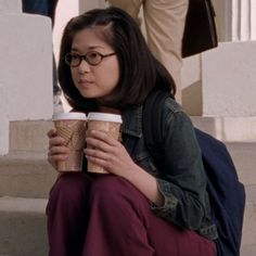 a woman sitting on the steps holding two coffee cups