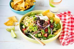 a salad in a bowl with tortilla chips on the side and a glass of water