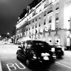 a black and white photo of cars driving down the street in front of a building