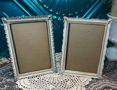 two old fashioned frames sitting on top of a doily covered table next to a vase