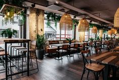 an empty restaurant with wooden tables and chairs in front of large windows, plants hanging from the ceiling