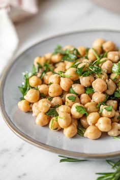 a plate full of chickpeas and parsley on a marble counter top with herbs