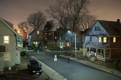 an empty street at night with some houses in the background and one car parked on the side