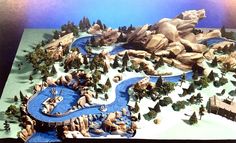 a model of a small town with mountains and trees in the foreground, along with a river running through it